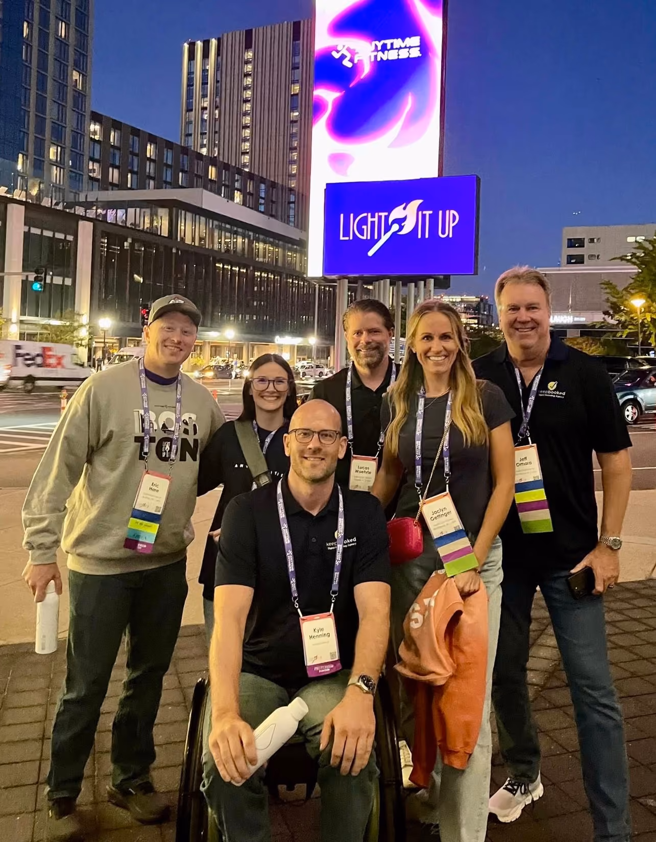 Group of six people posing outdoors at night near a lit sign reading Light It Up.