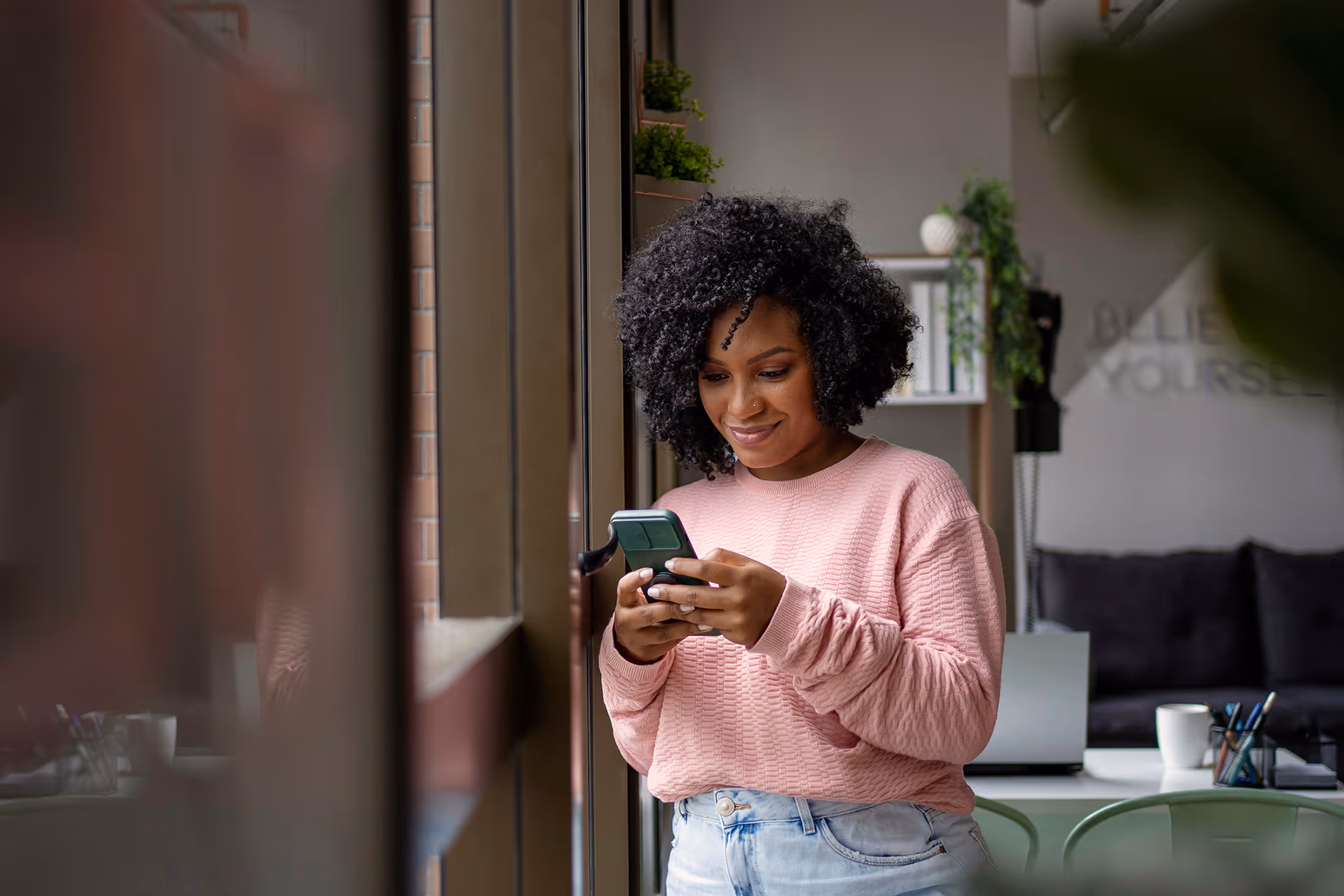 Woman smiling while using phone by a window in a modern room.