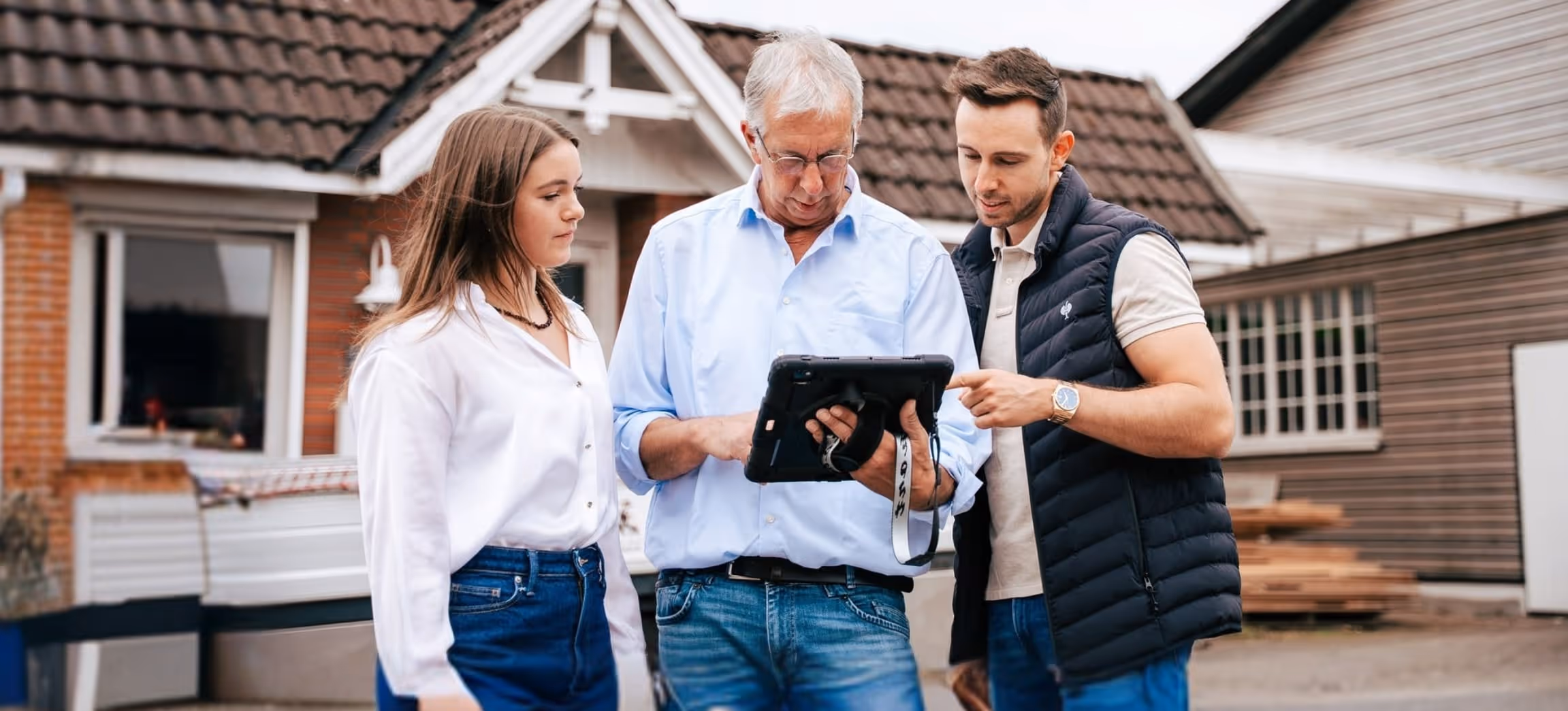 Drei Personen einer Familie stehen vor einem Haus und betrachten gemeinsam ein Tablet.