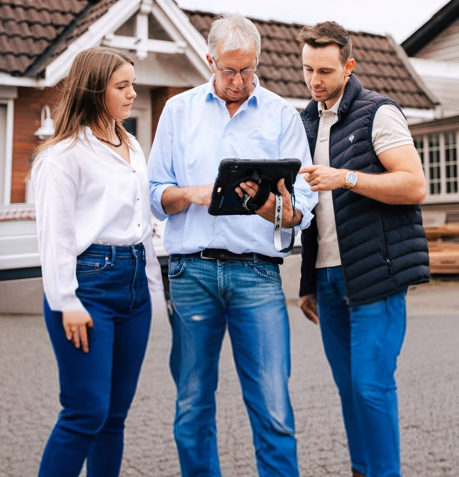 Drei Personen einer Familie stehen draußen vor einem Haus und schauen gemeinsam auf ein Tablet.