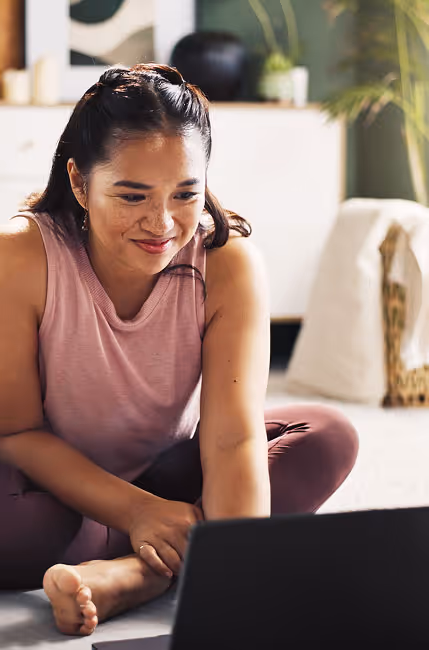 Smiling woman sitting cross-legged on the floor using a laptop in a bright, cozy room.