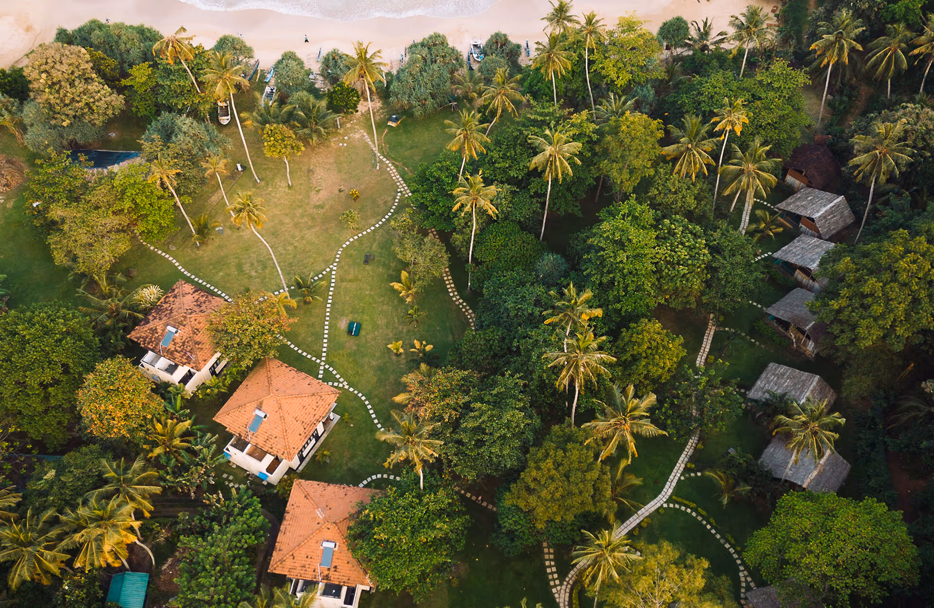 Aerial view of a tropical retreat venue with huts, palm trees and a sandy beach