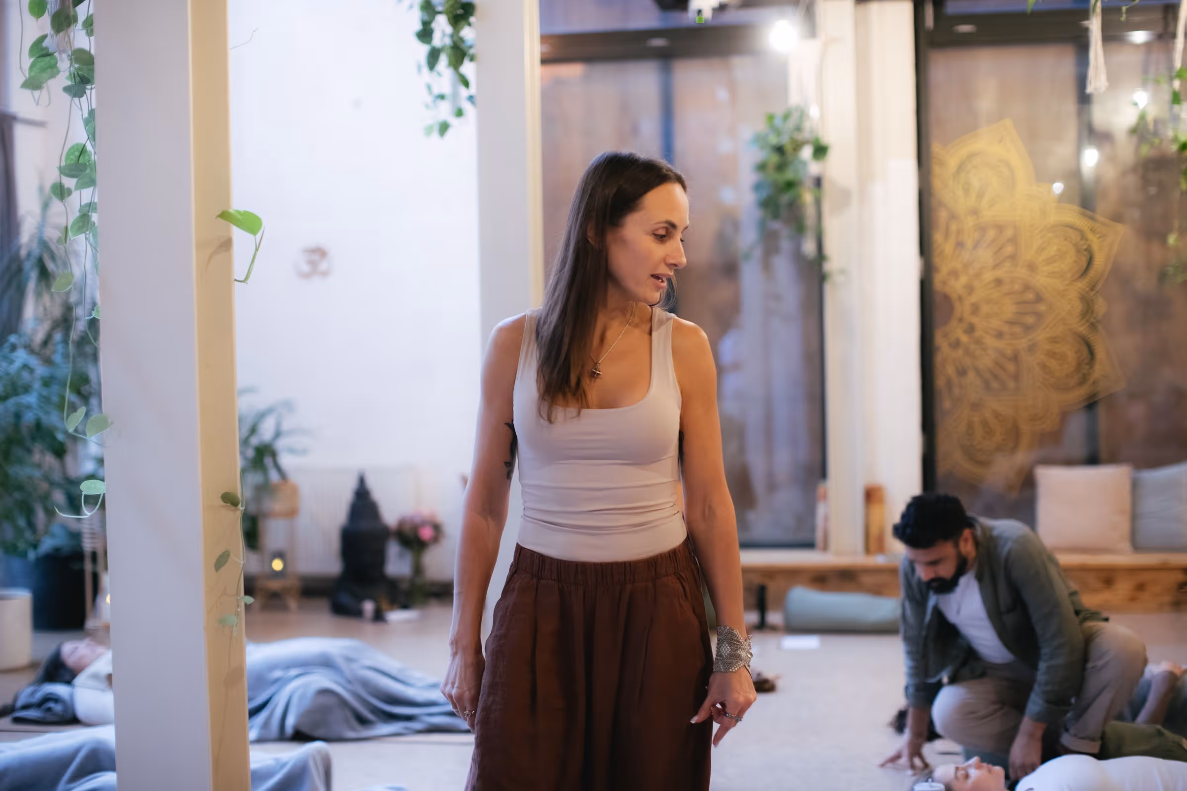 Woman standing and guiding a group session with people lying on the floor in a calm room.