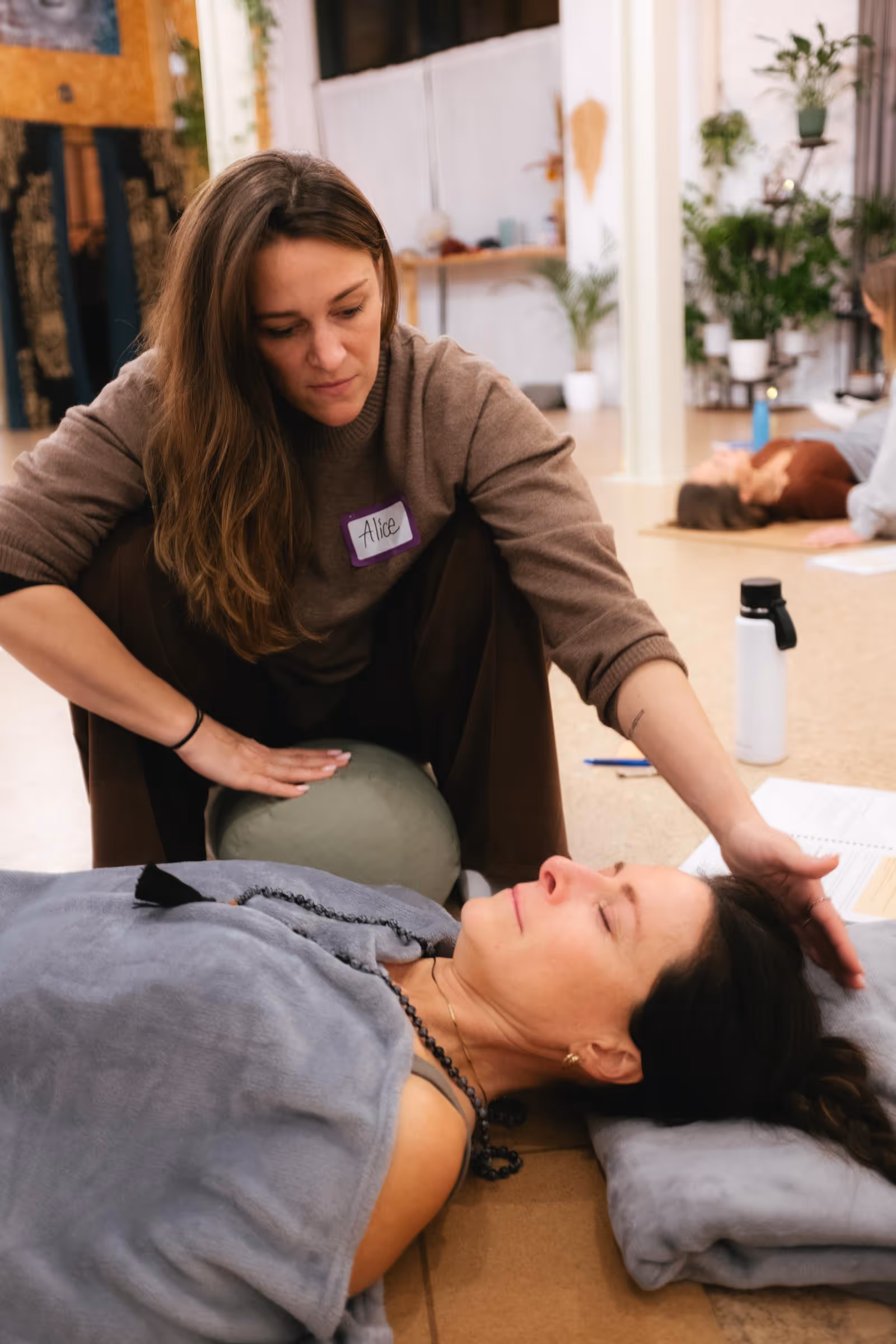 Woman named Alice gently touching the head of a reclining woman during a breathwork session.