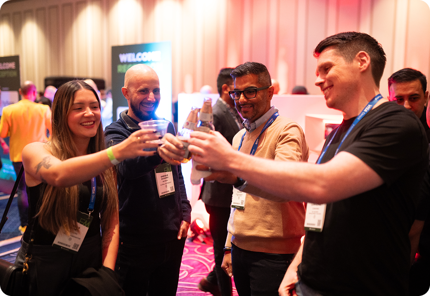 Four conference attendees clinking glasses and bottles in a celebratory toast at an indoor event.