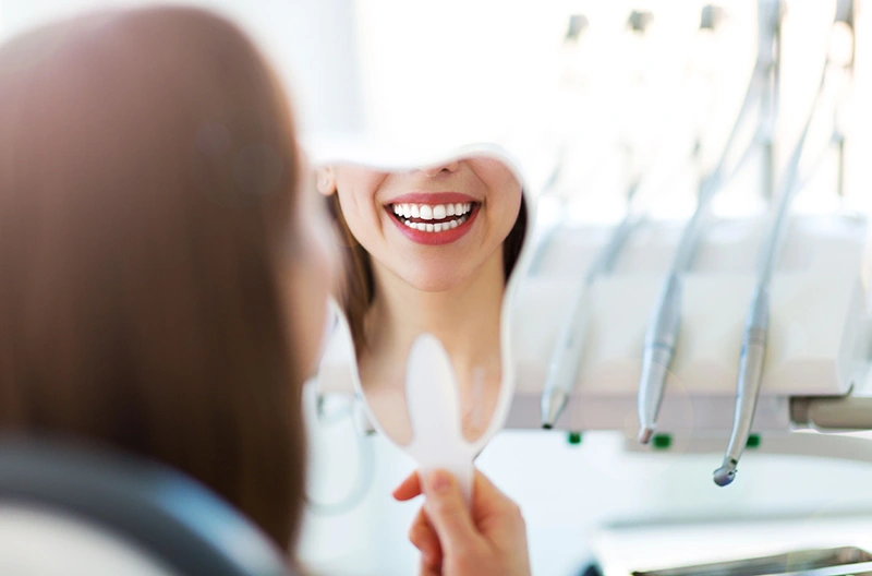 Dental professional in black uniform explaining clear aligner to a seated female patient in a dental office.