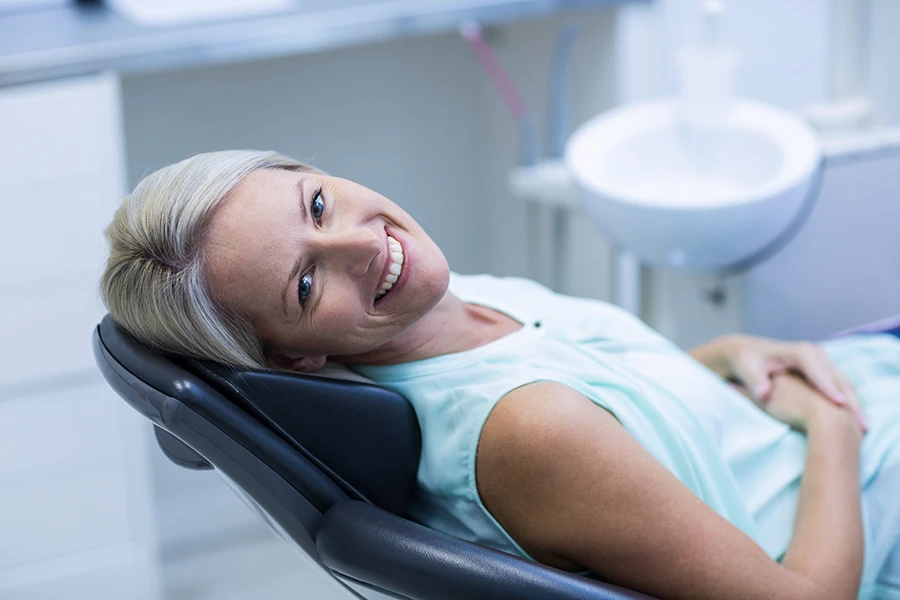 Smiling woman reclining in a dental chair in a clinic setting.