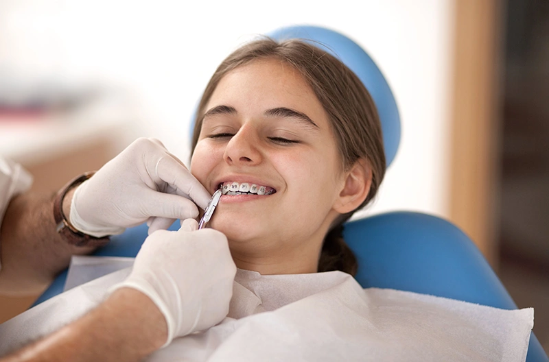 Teen girl with braces smiling while dentist adjusts her braces wearing white gloves.