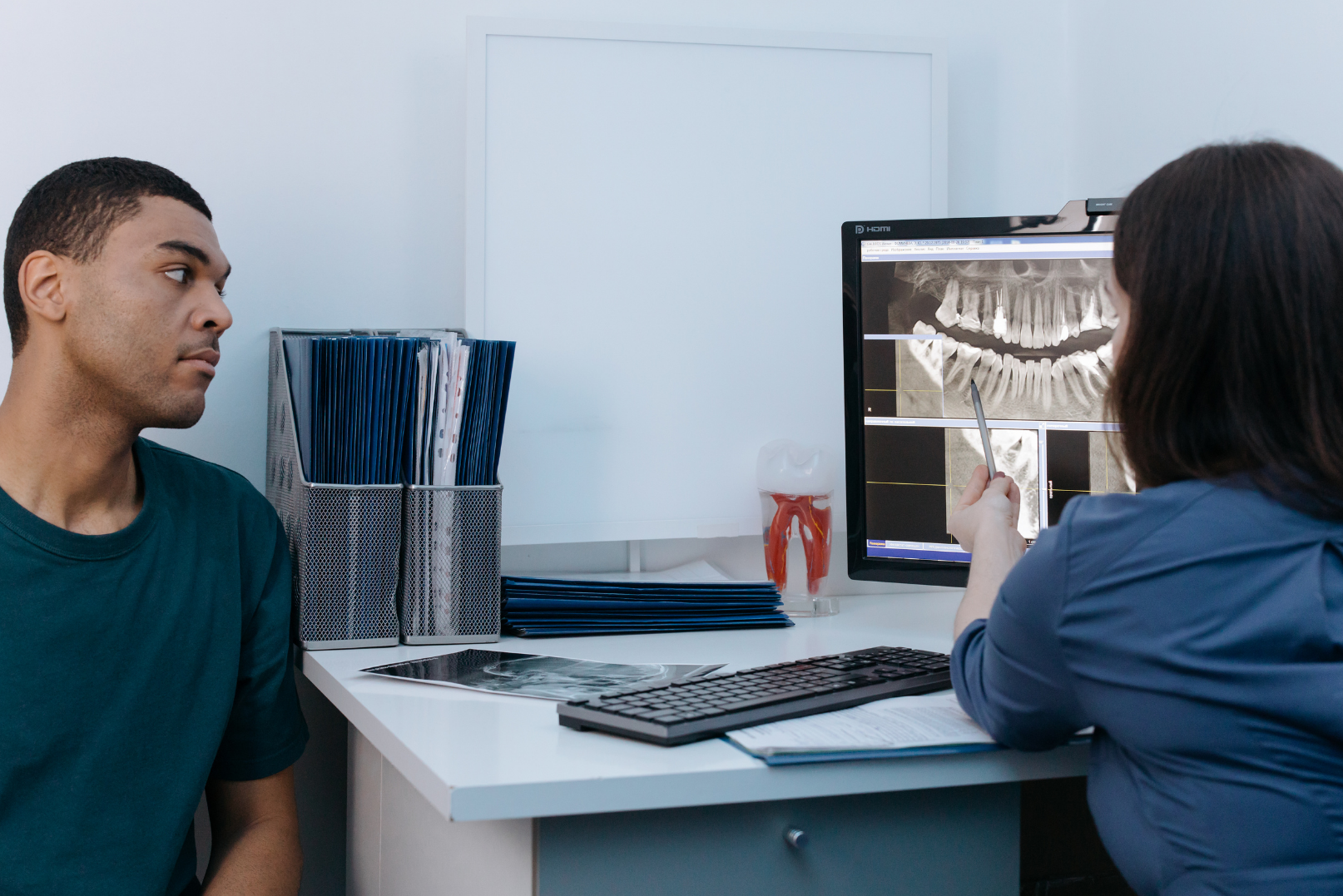 Dentist showing a male patient a dental X-ray on a computer screen in a consultation room.