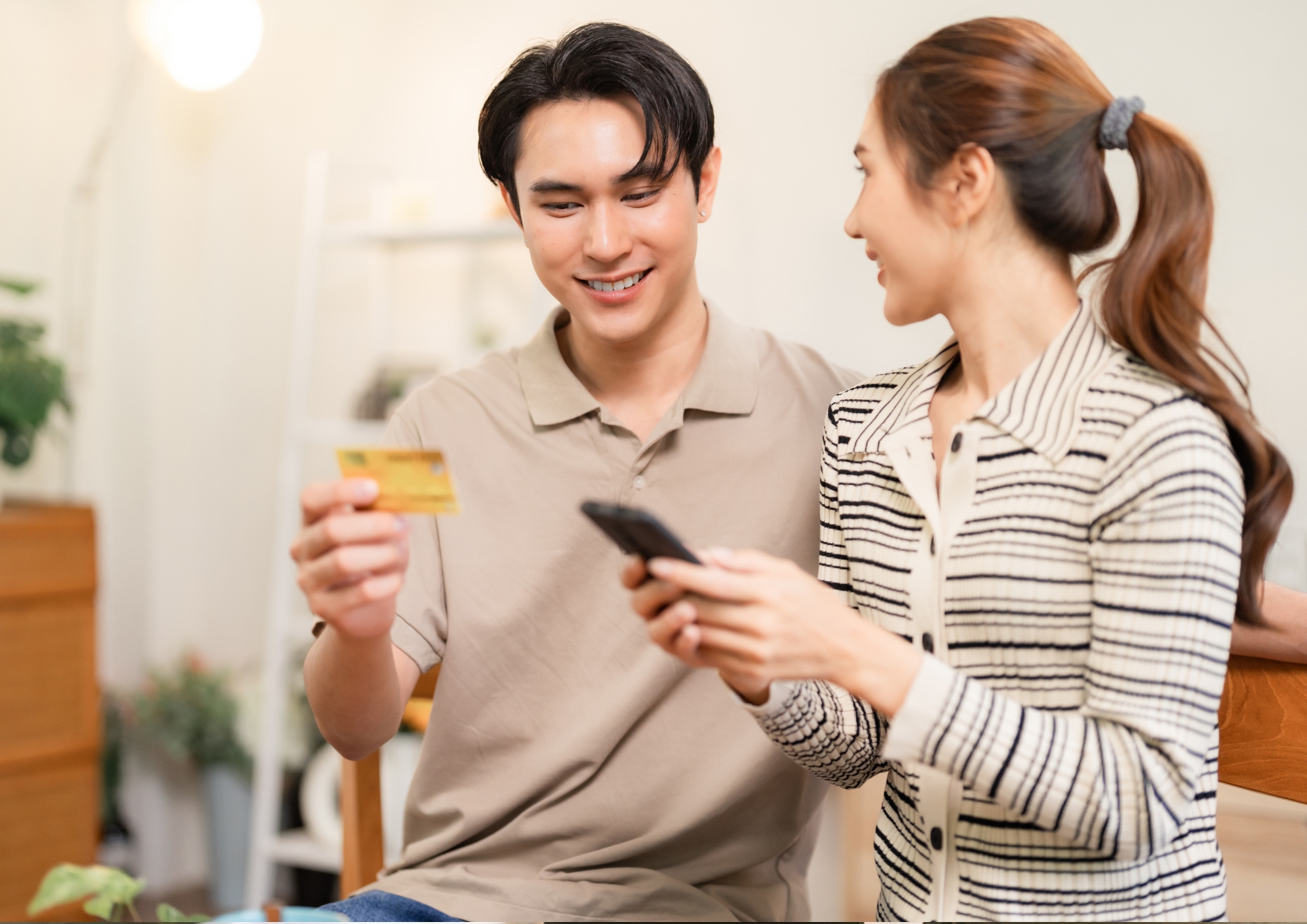 Man holding credit card and woman holding phone, smiling and interacting indoors.