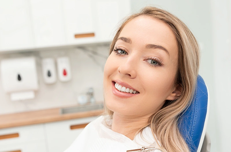 Smiling woman with blonde hair sitting in a dental chair in a modern clinic.