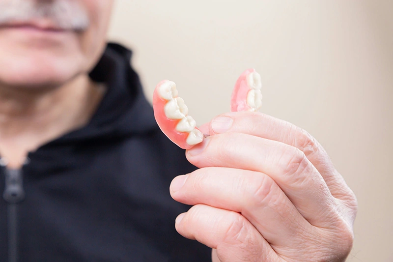 Man holding a pink dental bridge with artificial teeth between his fingers.