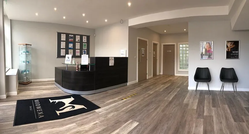 Modern lobby with black reception desk, display case, two chairs, and wood-look flooring.