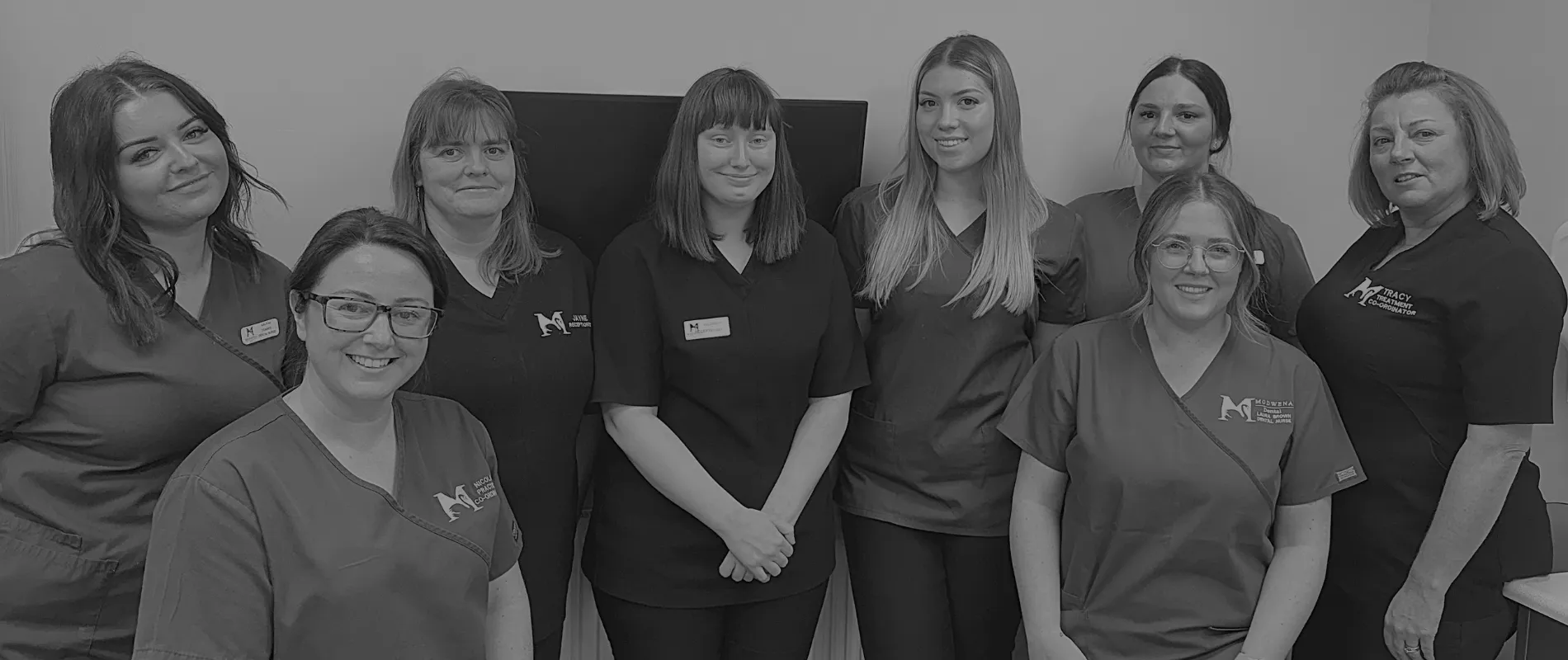 Group of eight women medical staff in scrubs posing and smiling indoors.