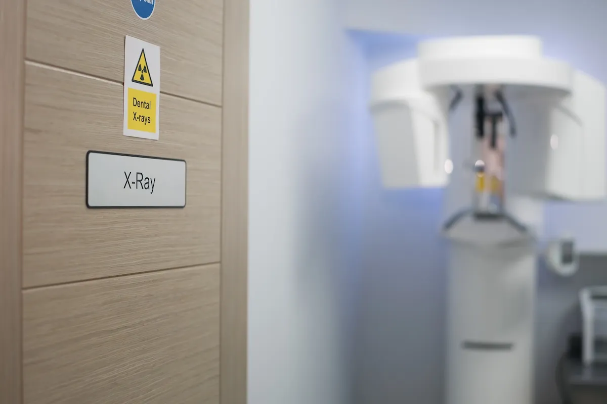 Wooden door with dental X-rays warning and X-Ray sign next to a blurred dental X-ray machine.