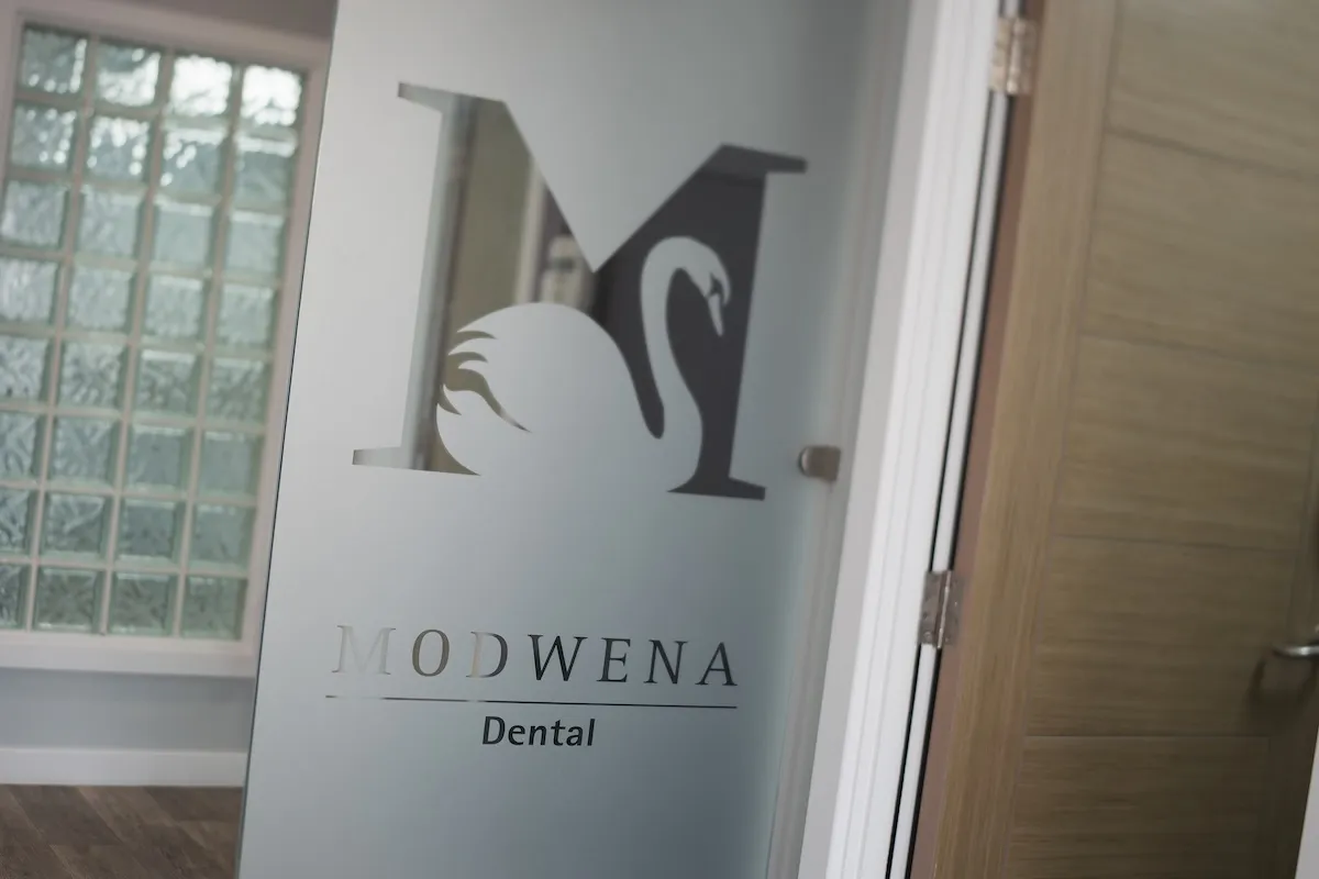Glass door with Modwena Dental logo featuring a swan and modern interior behind it.