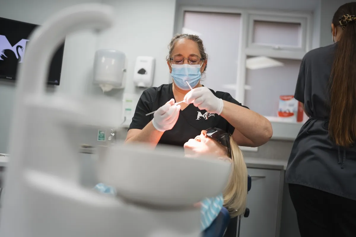 Dentist wearing mask and gloves treating patient lying back in dental chair with sunglasses on.