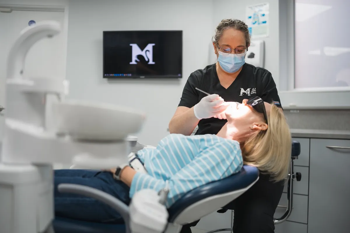 Dentist wearing mask and gloves treating a patient reclining in a dental chair.