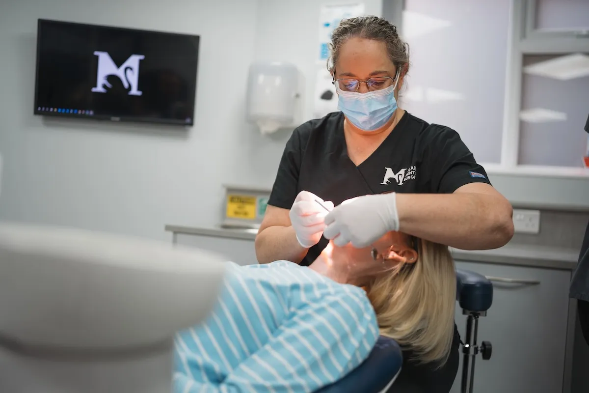 Dentist with mask and gloves examining a patient lying back in a dental chair.