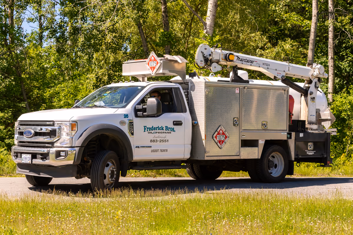 White Frederick Bros. propane service truck parked on a rural road beside trees and grass.