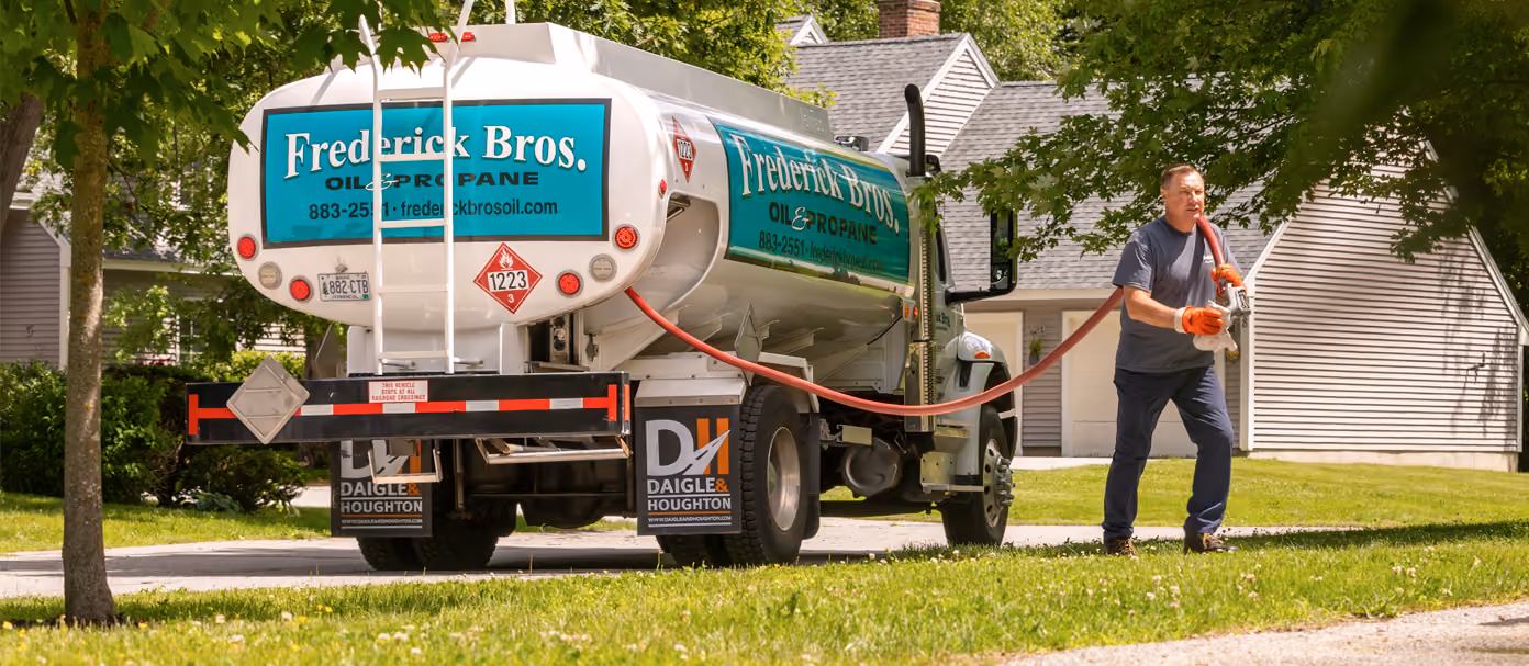 Fuel delivery truck parked outside a house while a worker handles a hose.