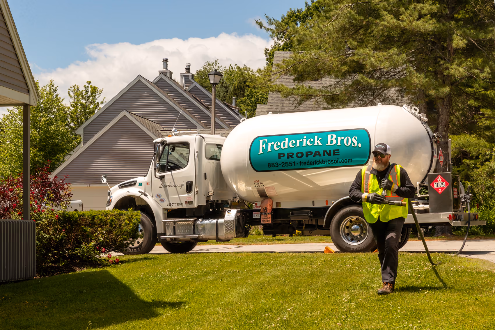 Propane delivery truck parked in a residential driveway while a worker carries a hose.