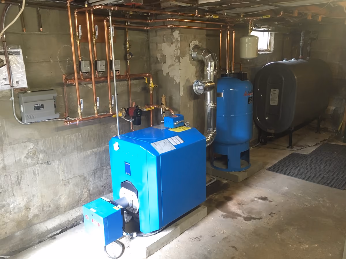 Basement utility room with an oil-fired boiler, copper piping, and two storage tanks.