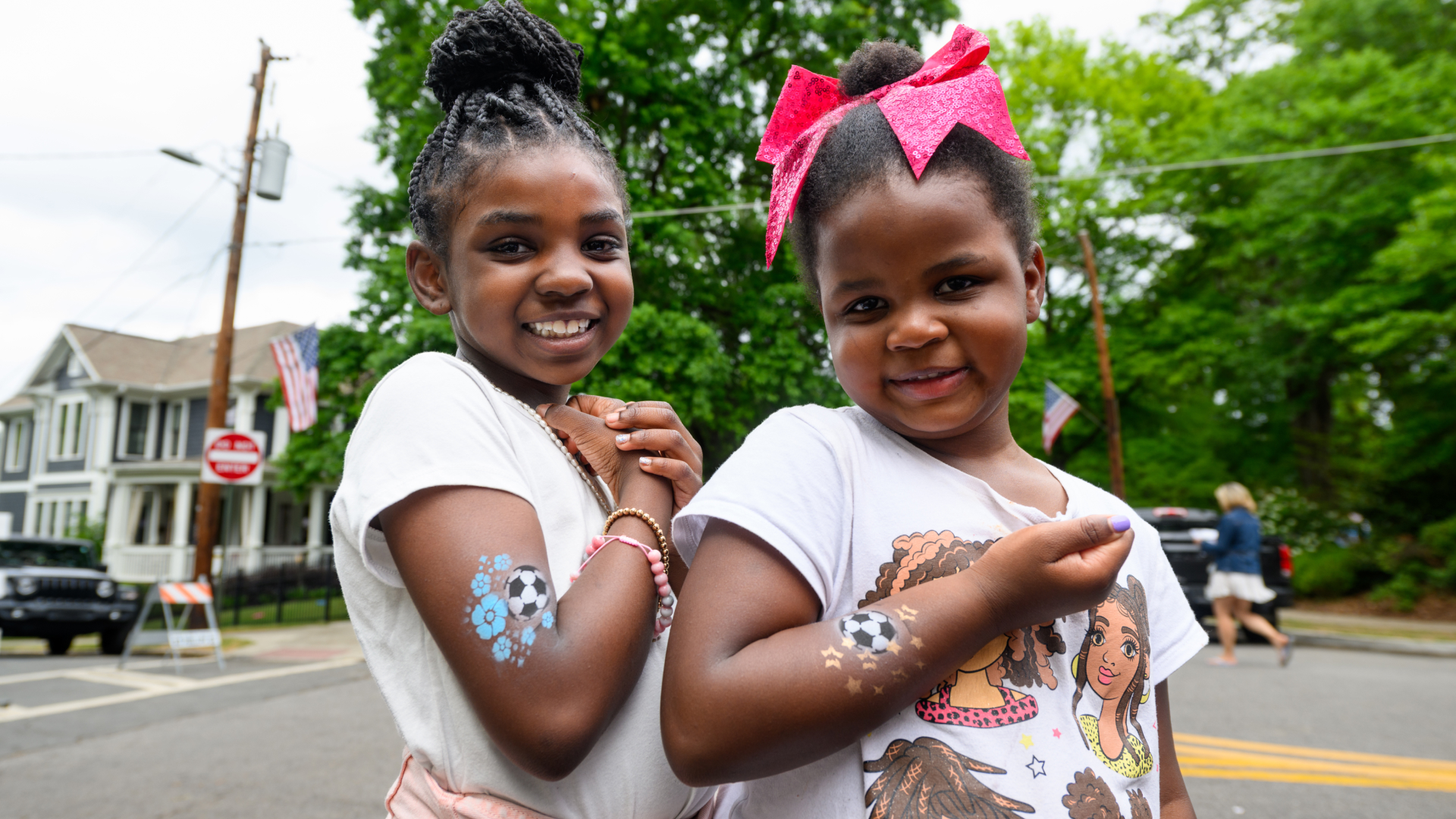 Two smiling girls showing soccer ball temporary tattoos on their arms outdoors.