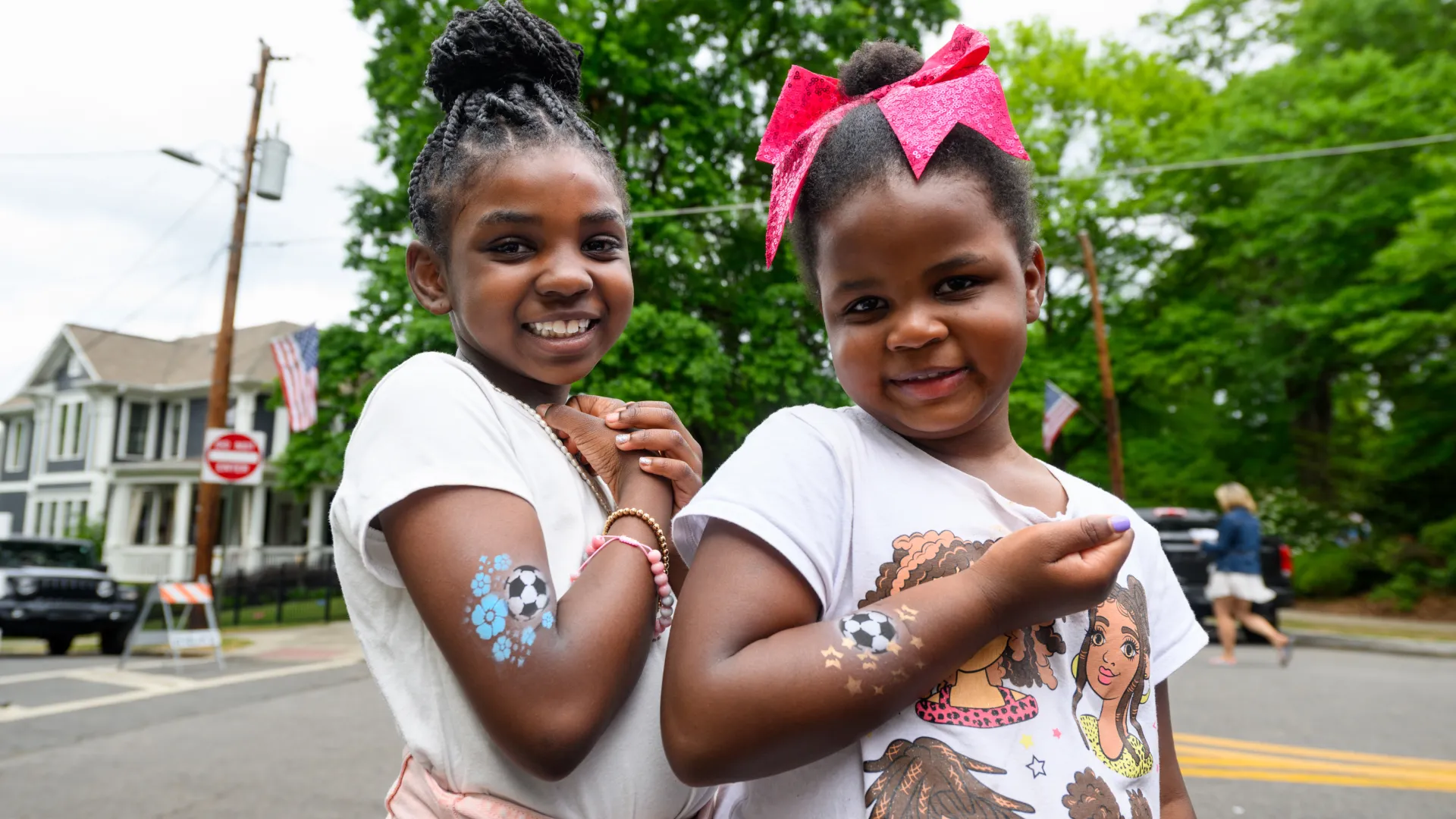 Two smiling girls showing soccer ball temporary tattoos on their arms outdoors.
