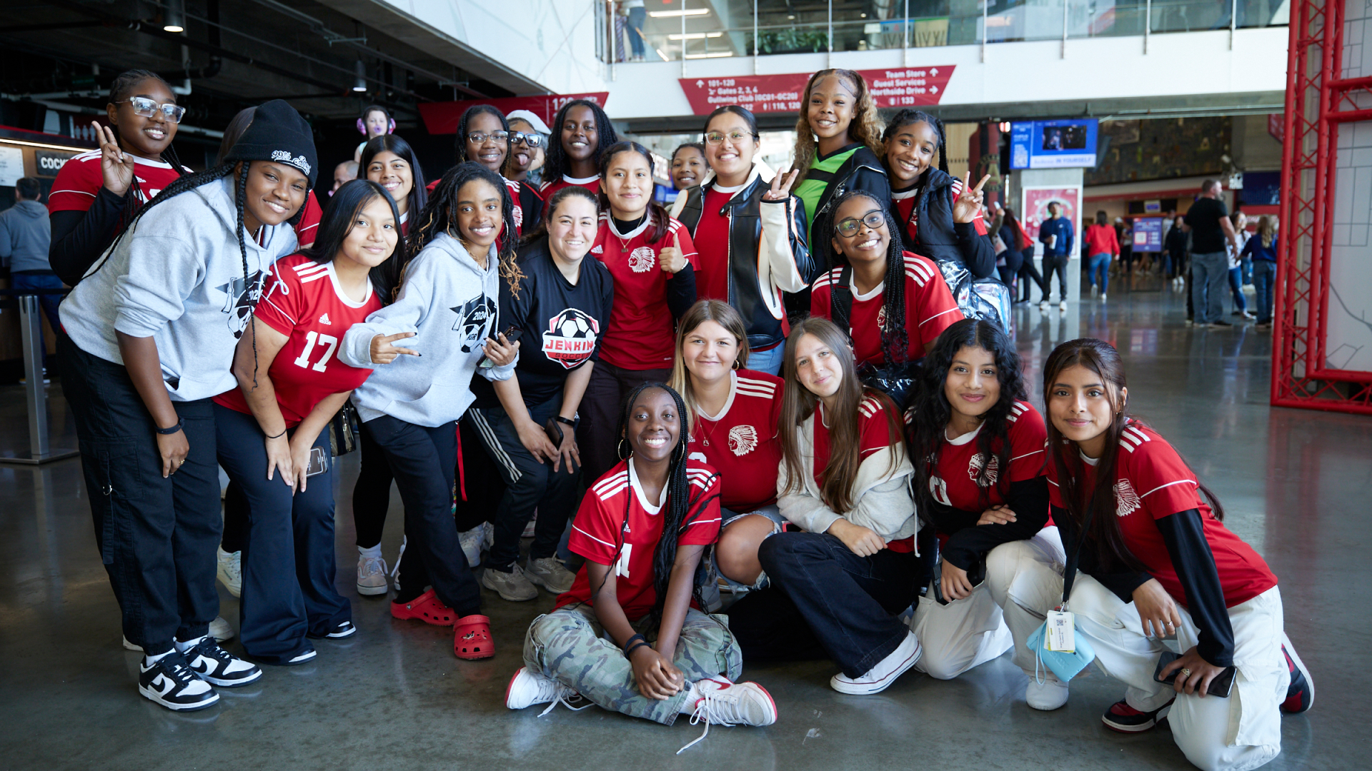 Group of young women wearing red sports jerseys posing indoors, some making peace signs and smiling.