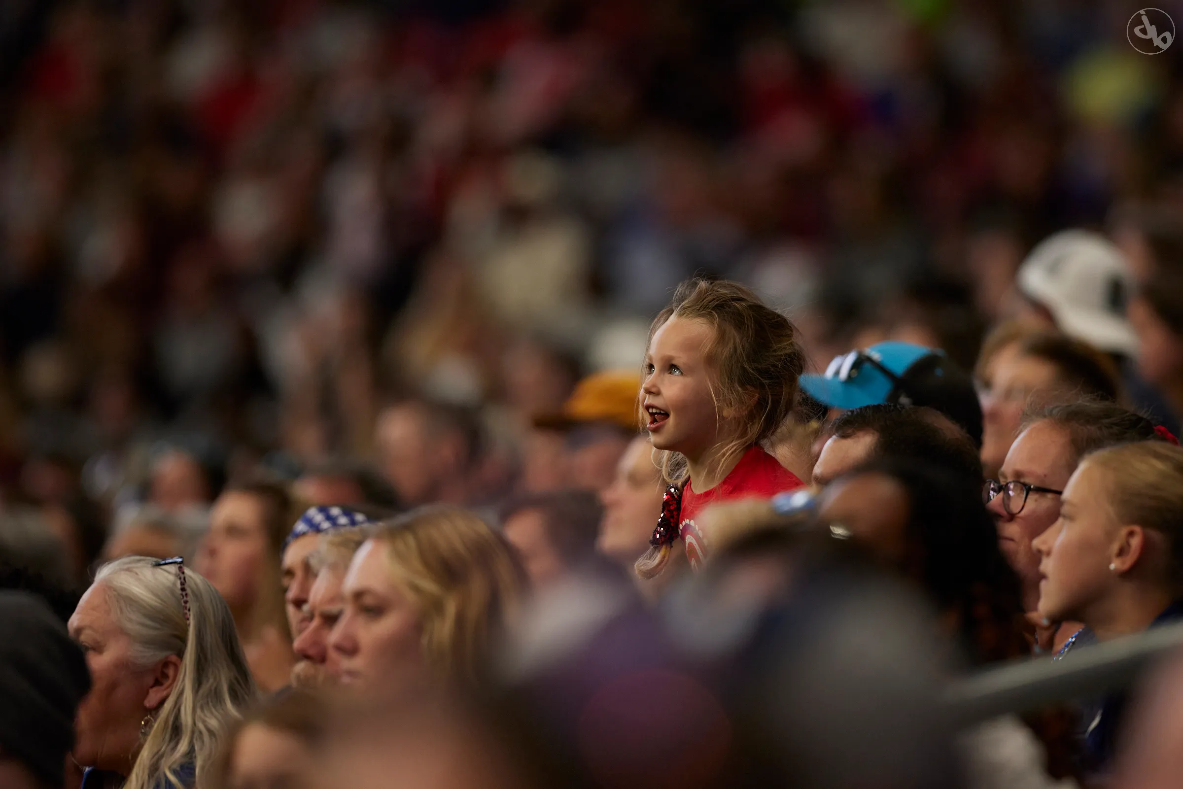 A young girl in a red shirt smiles in a crowd of fans in the stands.