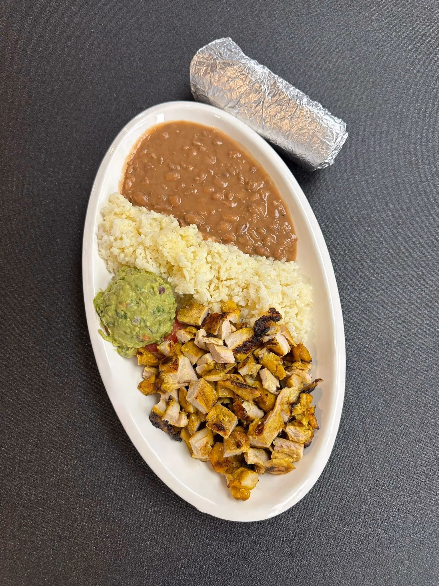 A plate of food with rice, beans, chicken, and guacamole.