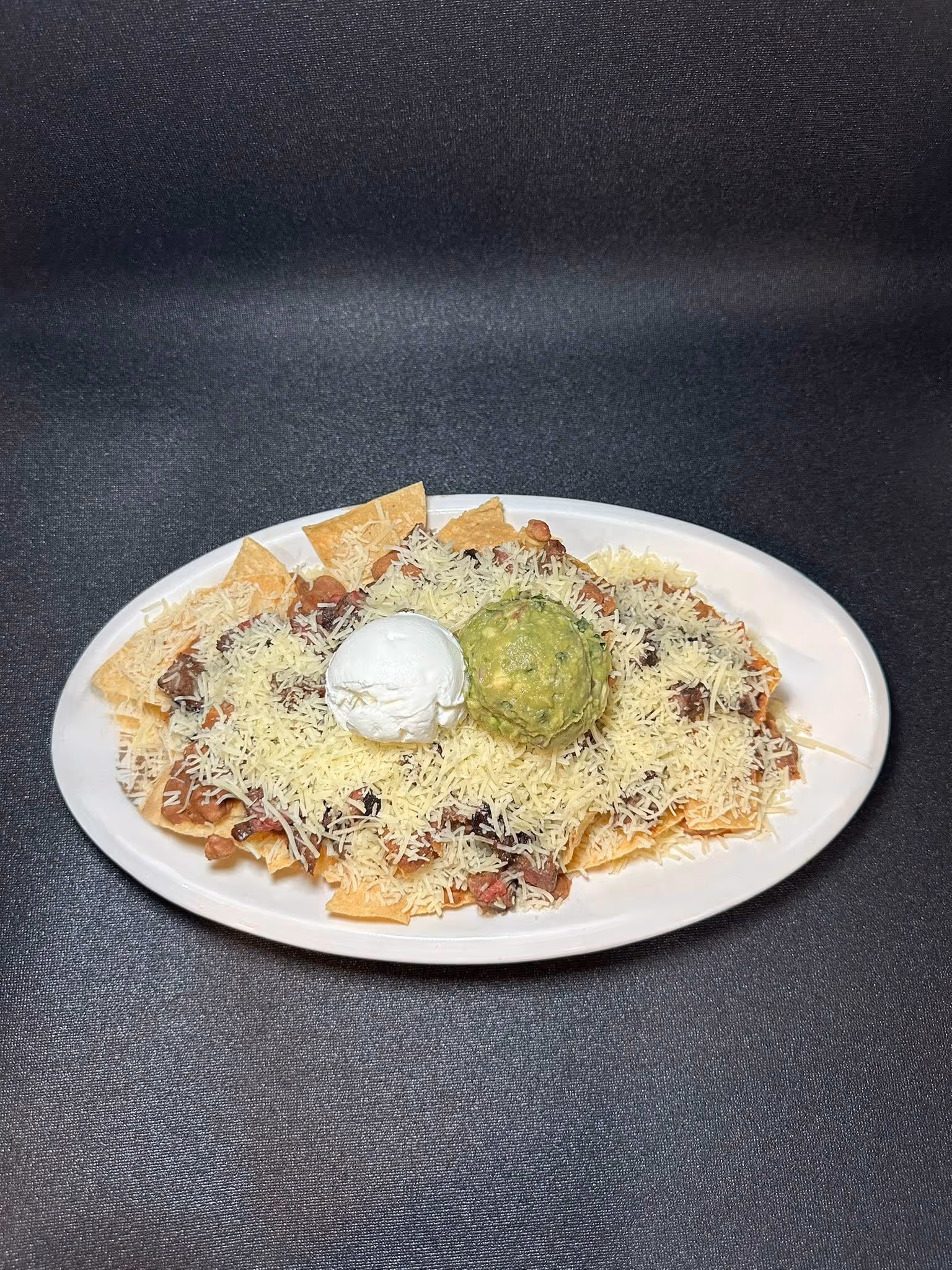 A plate of nachos with a white cheese sauce and a guacamole on top.