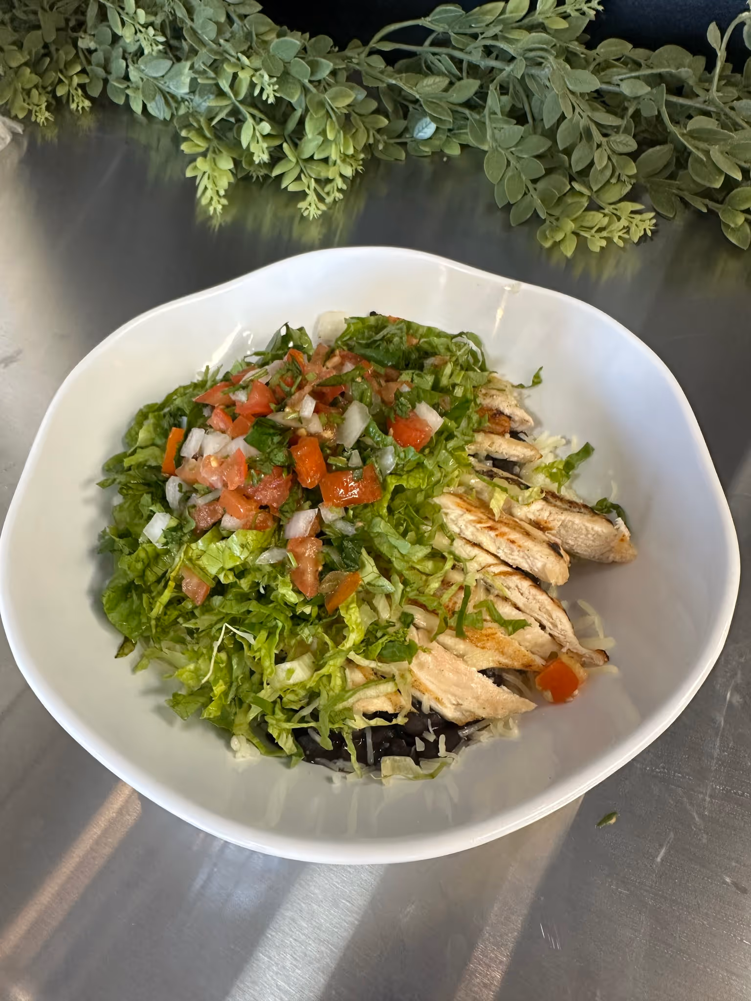 A white bowl filled with a salad of lettuce, tomatoes, and chicken.