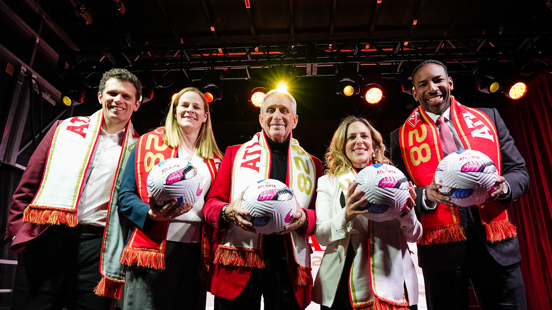Five people wearing Atlanta 28 scarves hold soccer balls on stage at the NWSL Atlanta expansion announcement.