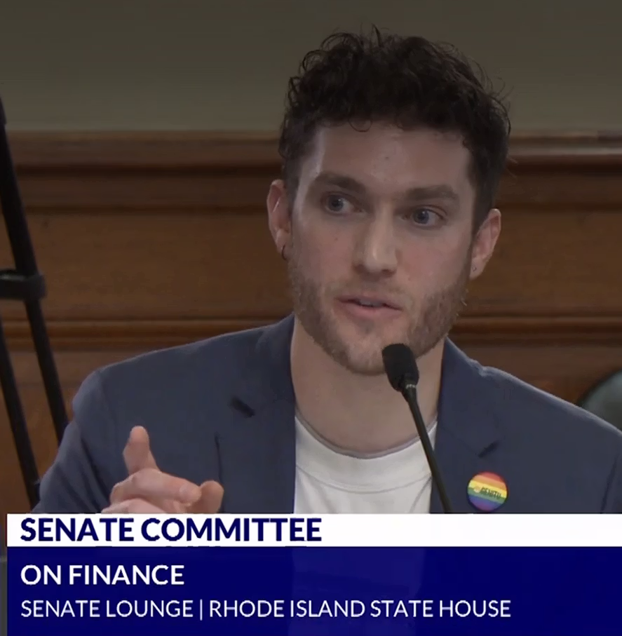 Jason speaking into a microphone at the Rhode Island State House Senate Committee on Finance session.
