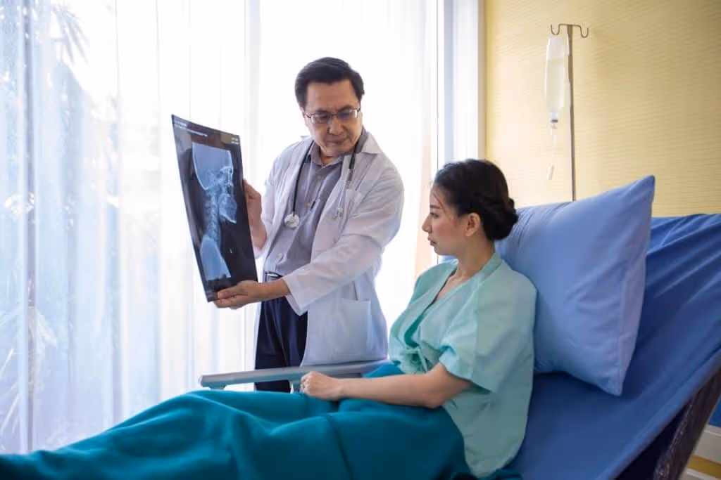 A female patient wearing a green gown sits in a hospital bed as her doctor explains the results of a brain scan.