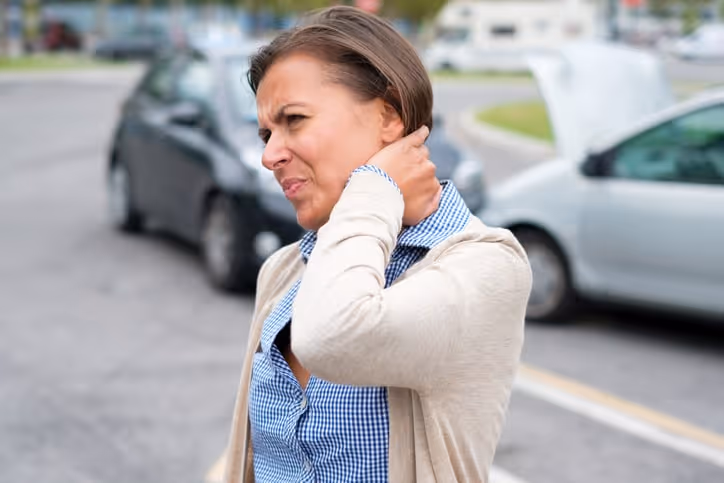 A woman winces in pain as she touches the back of her neck after a car accident.