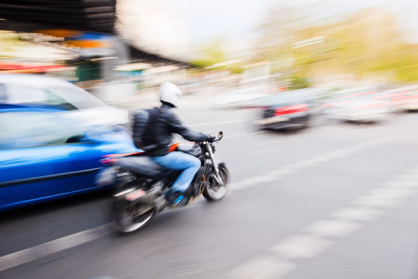 Blurred image of motorcyclist with white helmet driving through traffic