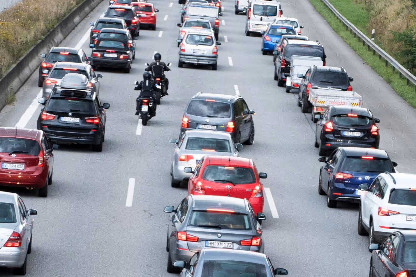 Two motorcycles dressed in black lane splitting between cars in traffic