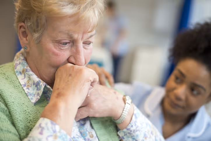 A nervous elder patient is shown being consoled by a concerned nursing home staff member.