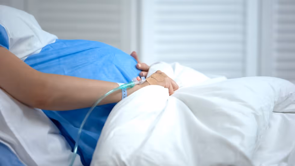 Pregnant woman holding abdomen while sitting up in a hospital bed