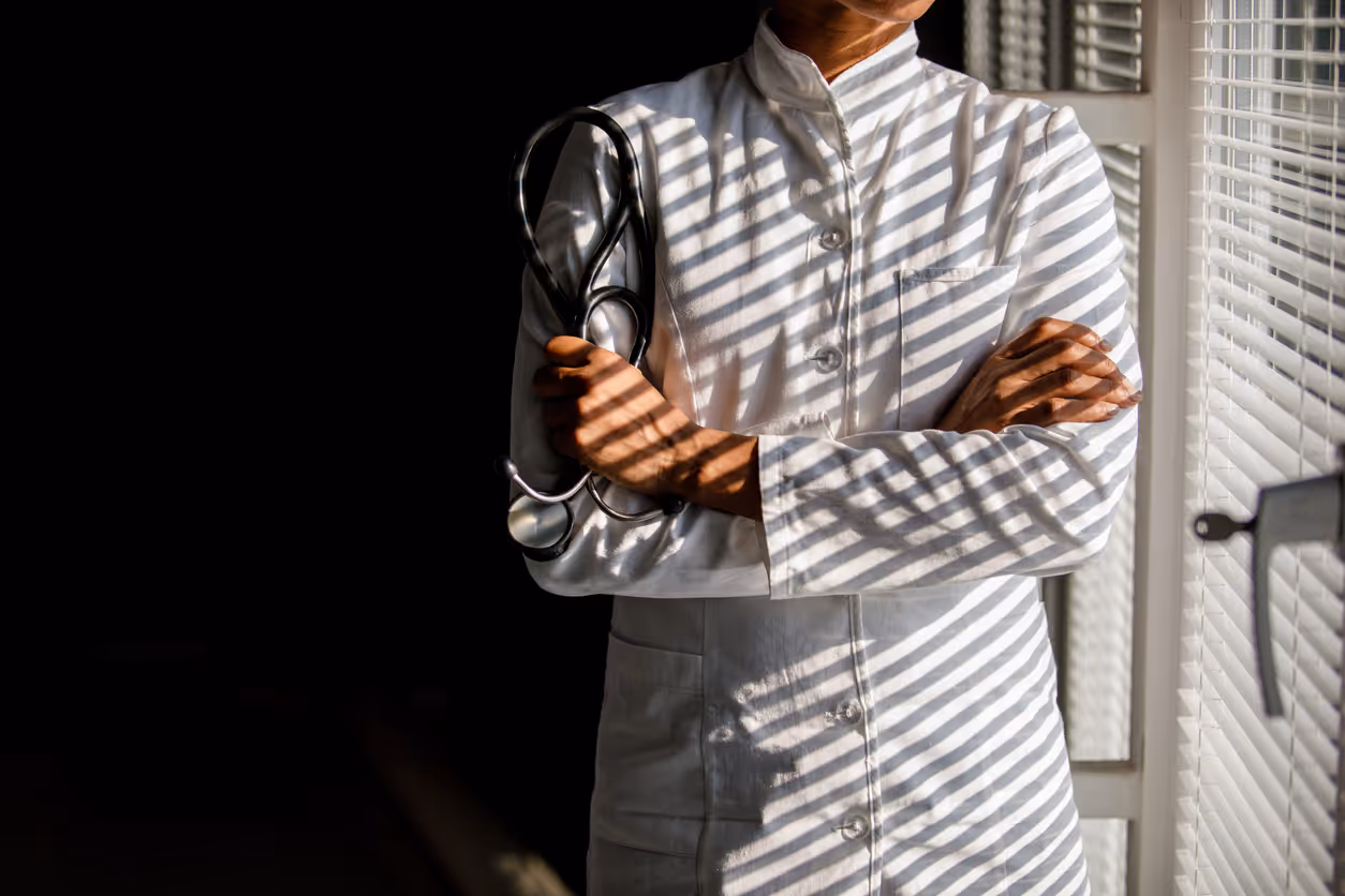 Doctor holding a stethoscope in the dark shadows by some blinds