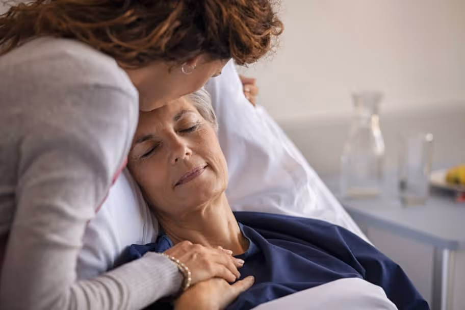 Woman comforts her mother who is in a hospital bed