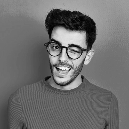 Young man with glasses winking and smiling in a black and white photo.