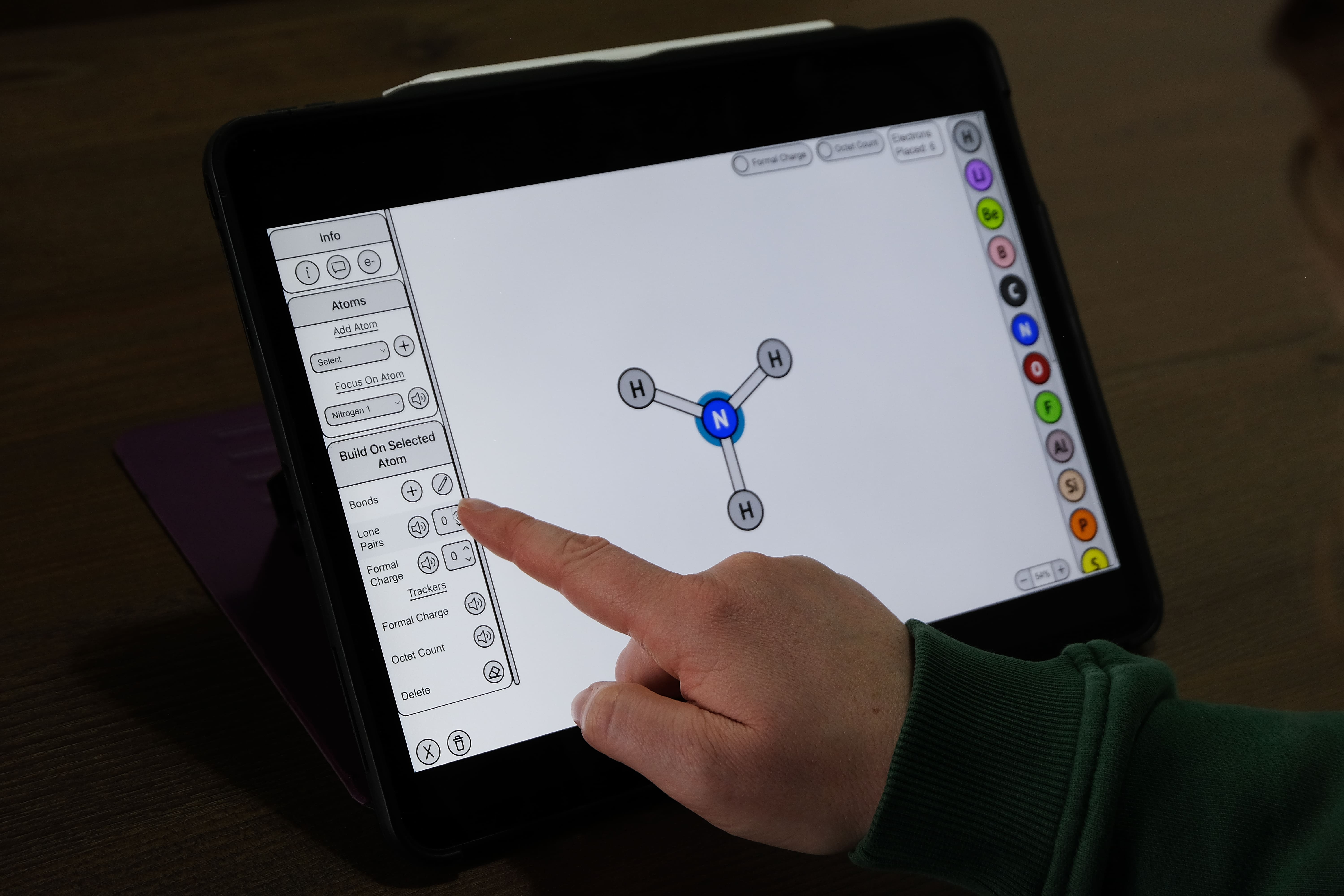 Hand touching a tablet screen with Alchemie's Lewis Structure tool and the keyboard accessible control panel (KACP) open. The user is using the control panel to build a molecular structure of ammonia (NH3).