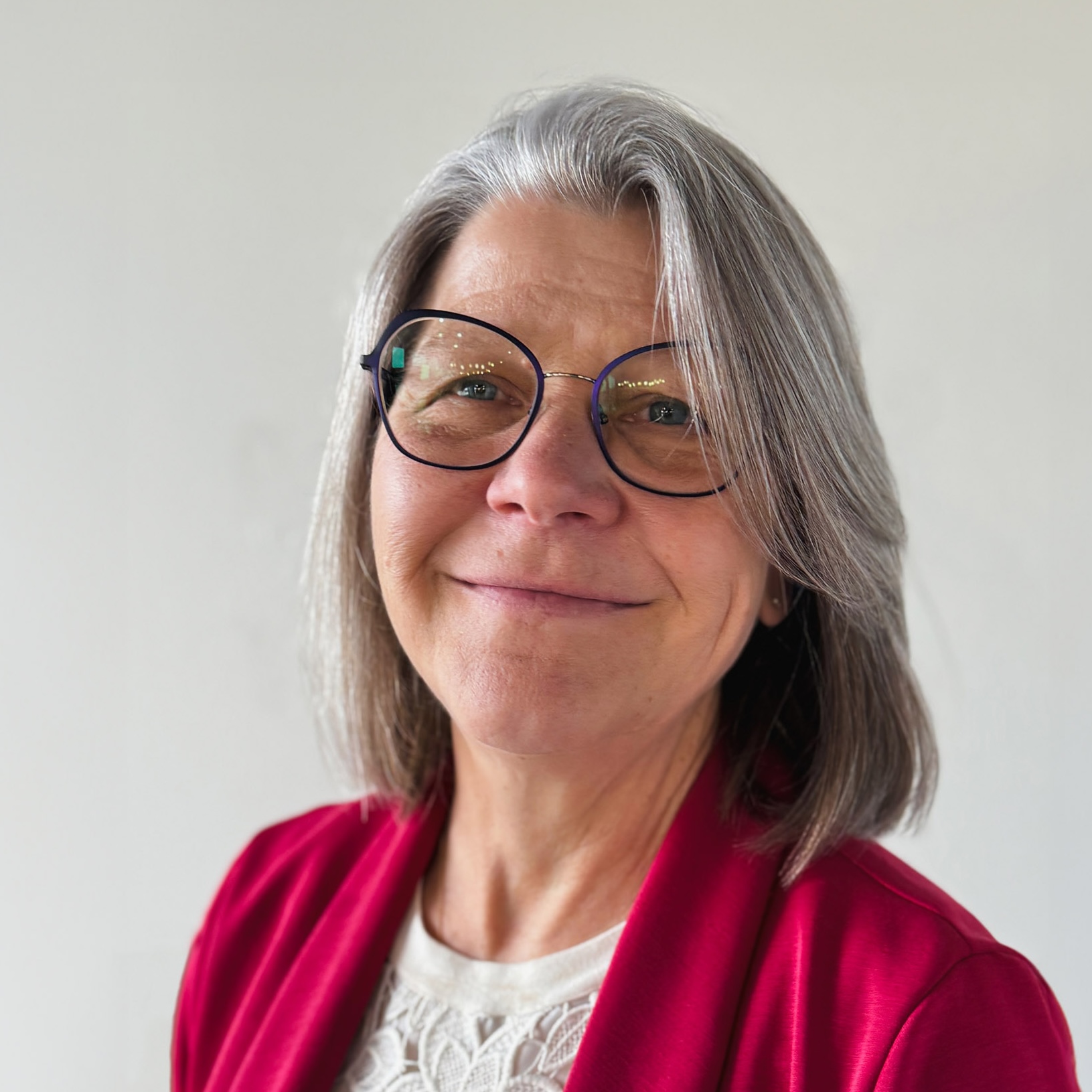 Julia Winter's headshot. Smiling middle-aged woman with glasses wearing a red jacket in front of a plain light background.