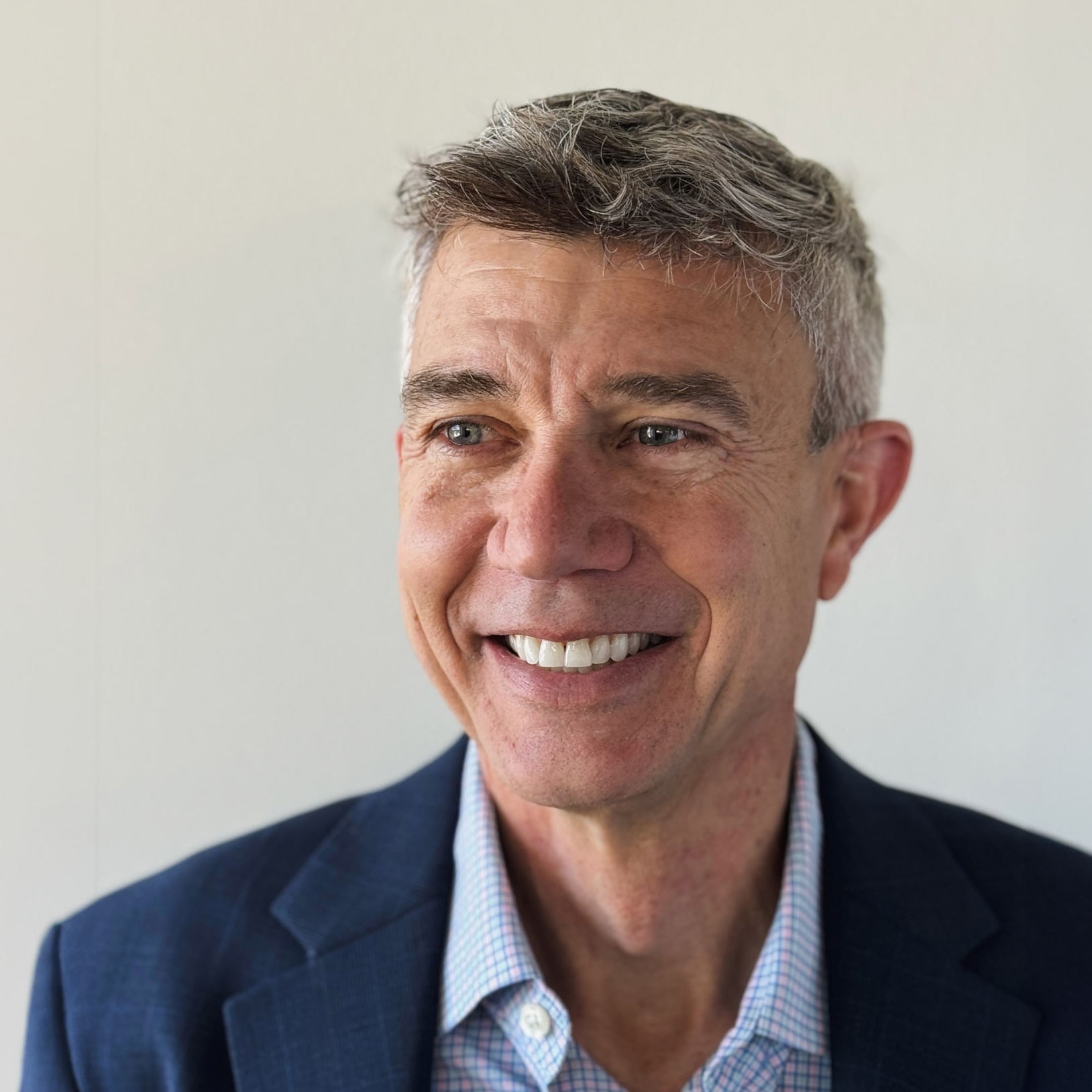 Carl Rundell's headshot. Smiling middle-aged man wearing a blue blazer against a plain light background.