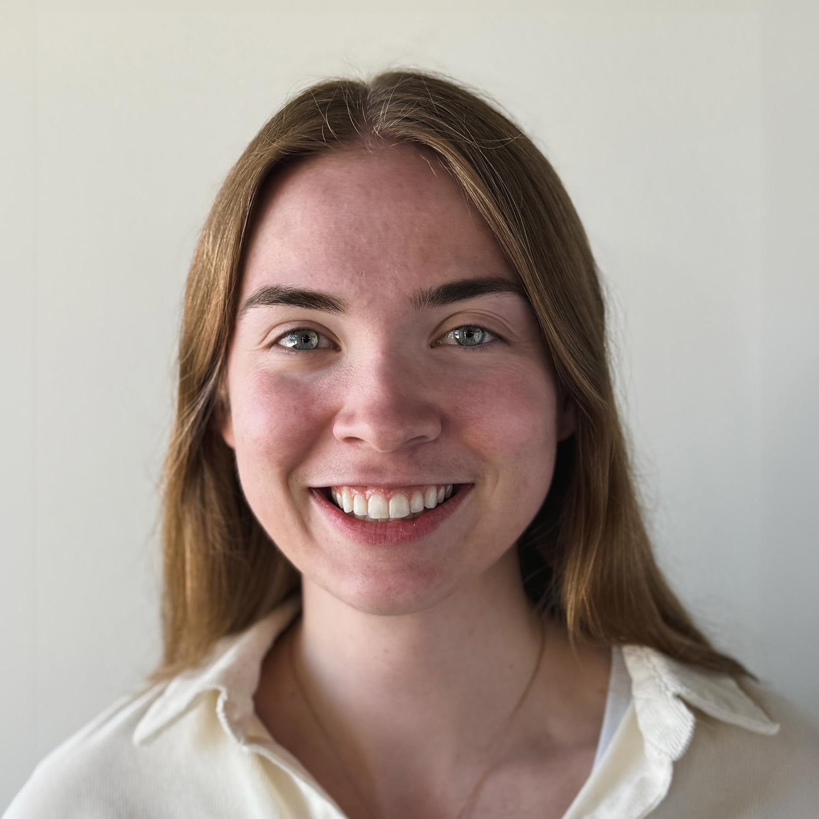 Katherine Rochon's headshot. Smiling young woman with long light brown hair and green eyes wearing a cream-colored collared shirt.