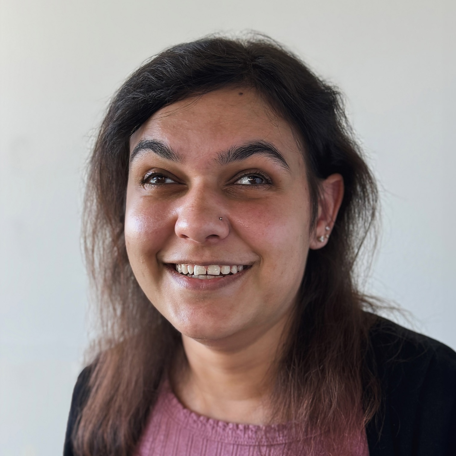Nicole Kada's headshot. Smiling woman with dark hair wearing a pink top and black cardigan against a plain light background.